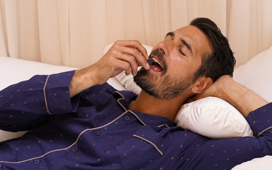 Man reclining on a bed taking a CBD gummy in a calm bedroom setting