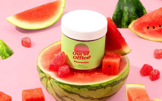 Front of Out of Office watermelon gummies jar with green label and white lid, surrounded by watermelon slices and red gummies