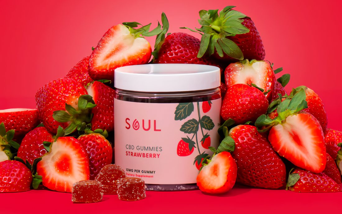 Front view of Soul strawberry CBD gummies jar showing label and gummy pieces among fresh strawberries on red background