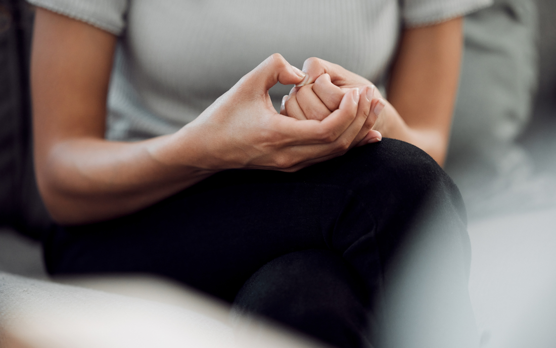 Person sitting on a couch with hands clasped in their lap, close-up conveying anxiety and introspection