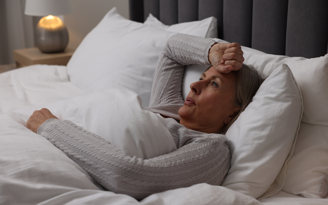 Middle-aged woman lying in bed holding her forehead and looking restless in a softly lit bedroom