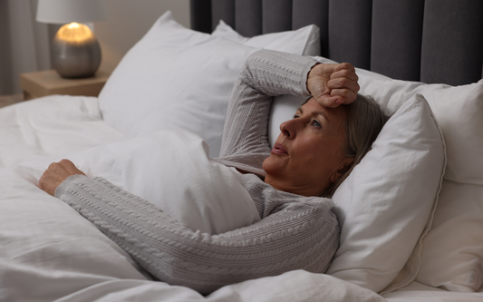 Middle-aged woman lying in bed holding her forehead and looking restless in a softly lit bedroom