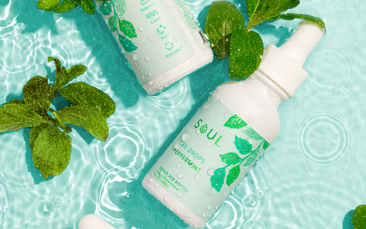 Angled top view of Soul peppermint CBD drops bottle showing label and dropper on rippling turquoise water with fresh mint leaves