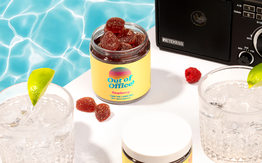 Angled view of Out of Office raspberry gummies jar open to show gummies on a white table with drinks and a speaker