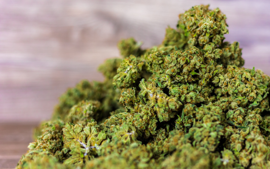 Close-up of dried cannabis buds piled on a wooden surface with a blurred wood background
