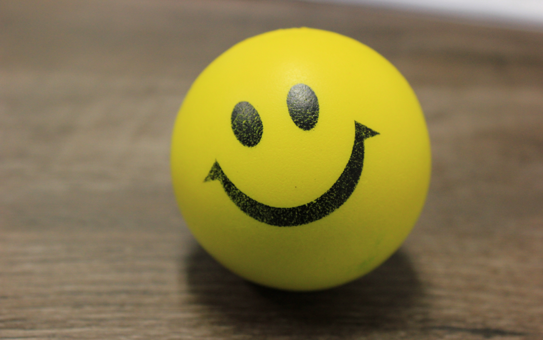 Yellow stress ball with a black smiley face on a wooden table, symbolizing mood and well-being