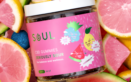 Angled close-up of Soul CBD Gummies jar showing the pink ‘Seriously Sour’ label, flavor icons, and sliced citrus background