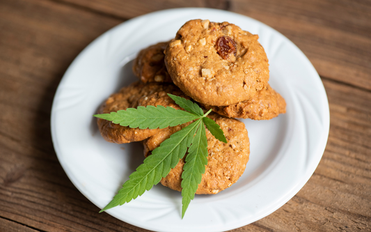 Three CBD cookies stacked on a white plate topped with a cannabis leaf on a wooden table