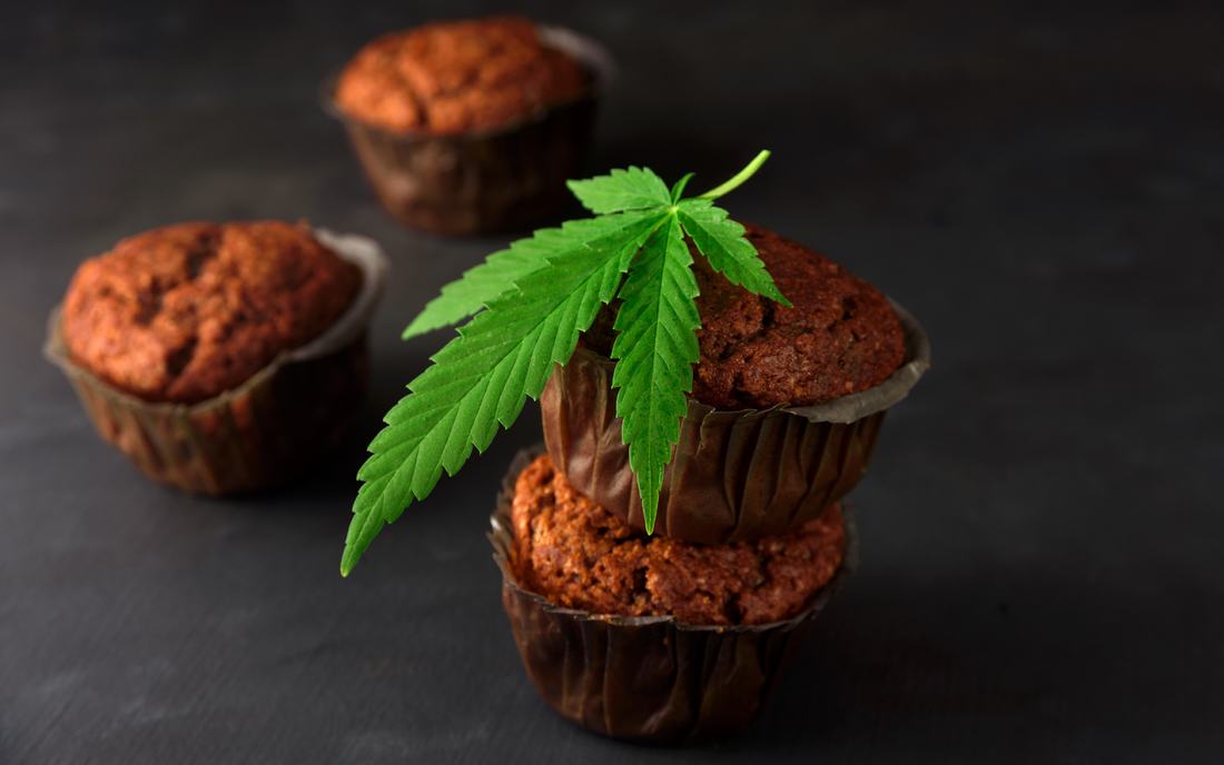 Three chocolate muffins topped with a cannabis leaf on a dark tabletop