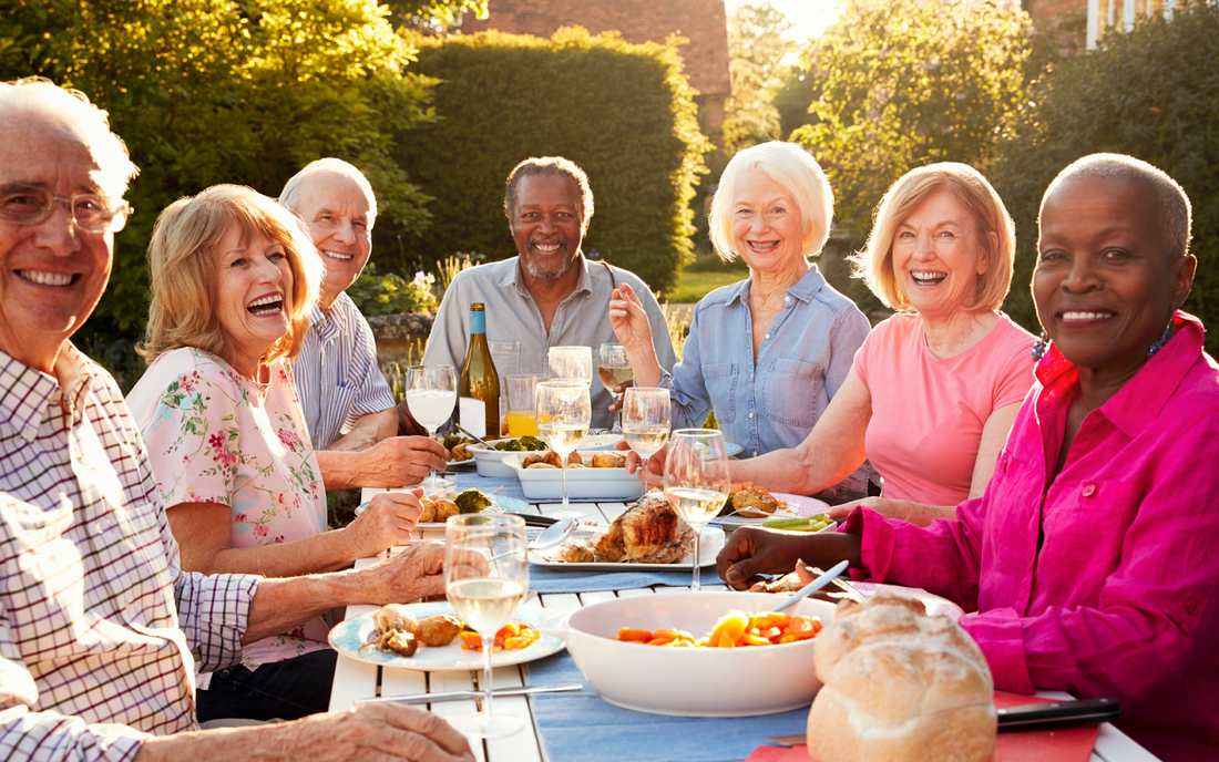 Group of older adults enjoying a sunlit outdoor meal together at a garden table