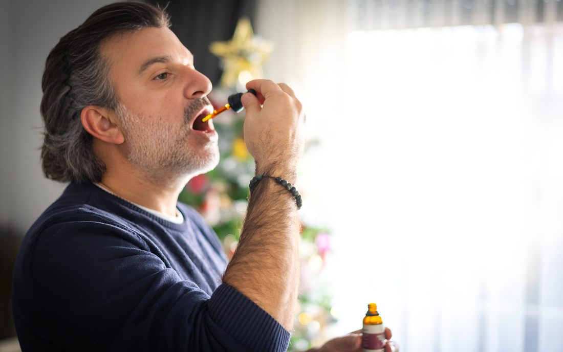Hombre tomando aceite de CBD con un cuentagotas frente a un árbol de Navidad en una sala iluminada