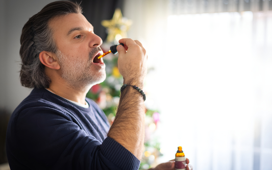 Hombre tomando aceite de CBD con un cuentagotas frente a un árbol de Navidad en una sala iluminada