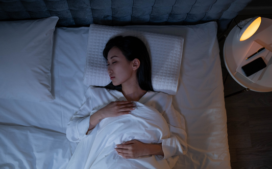 Mujer dormida de lado en la cama por la noche, con una mesita y lámpara encendida a su lado
