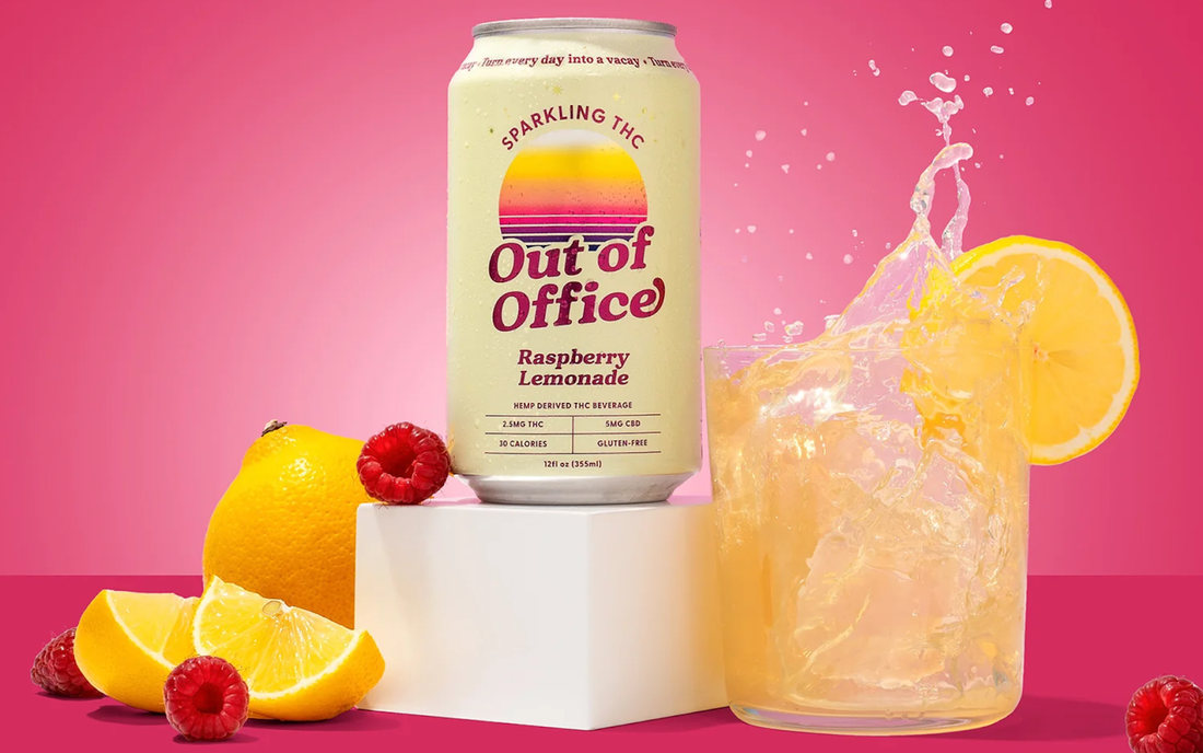 Front view of Out of Office Raspberry Lemonade can next to a splashing glass, lemon and raspberries on pink background