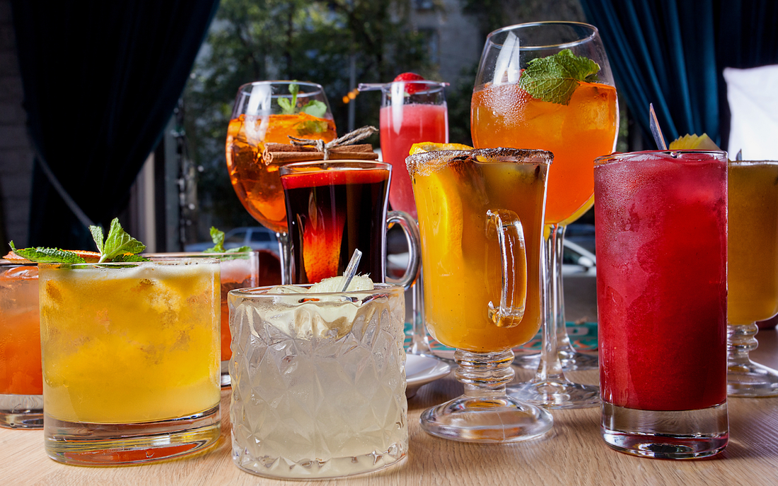 Colorful THC-infused cocktails and mocktails on a wooden table, garnished with mint and citrus, window and curtains behind