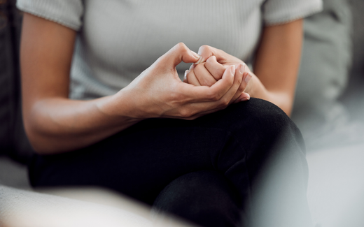 Person seated on a couch with hands clasped in their lap, conveying anxiety or contemplation