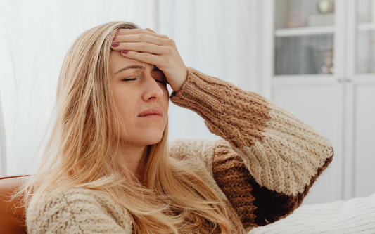 Woman clutching her forehead in pain on a couch in a bright living room, appearing to have a headache