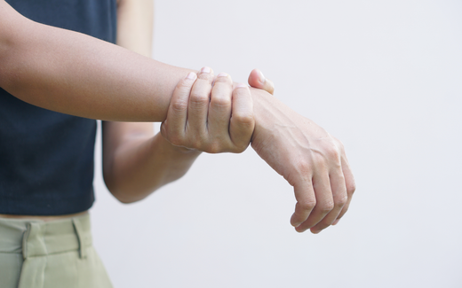Close-up of a person holding their wrist with the other hand, indicating nerve or wrist pain against a plain light background