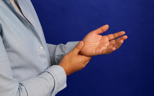 Person holding their wrist with the other hand, palms facing up against a solid blue background suggesting hand or wrist pain