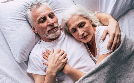 Older couple cuddled together asleep in bed, peaceful bedroom setting