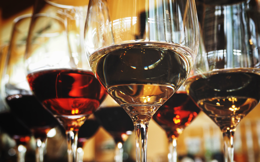 Close up of wine glasses with red and white wine on a bar reflecting warm ambient light