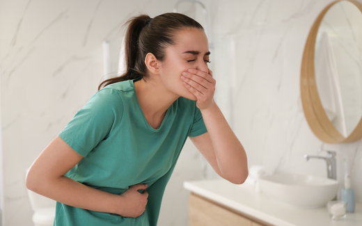 Young woman holding her stomach and covering her mouth in a bathroom, appearing nauseous