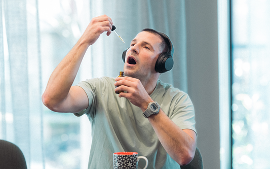 Man taking CBD oil from a dropper while wearing headphones at a bright table