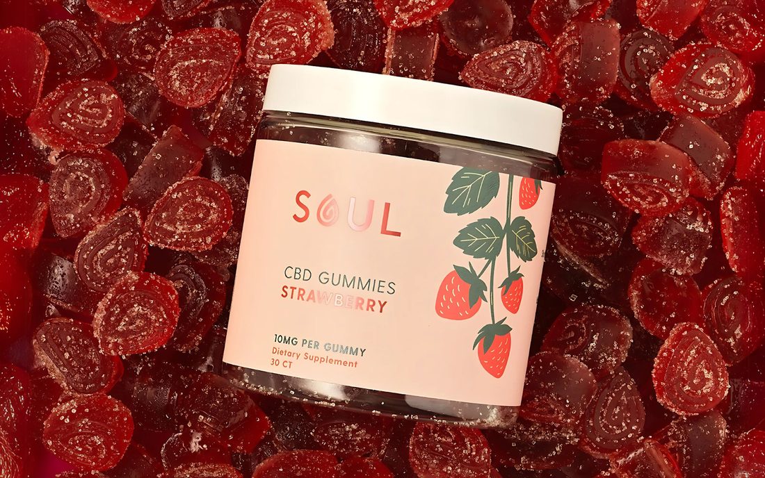 Angled top view of Soul strawberry CBD gummies jar showing pink label stating 10mg per gummy and white lid on a bed of sugar-coated red gummies