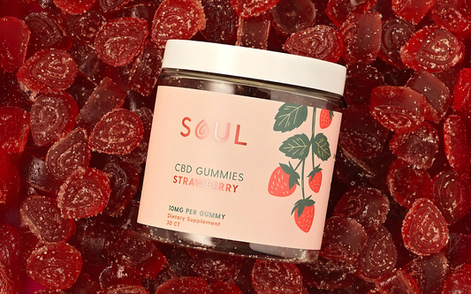 Angled top view of Soul strawberry CBD gummies jar showing pink label stating 10mg per gummy and white lid on a bed of sugar-coated red gummies