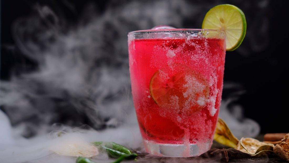 Close-up of a red mocktail in a glass showcasing crushed ice, a salted rim and a lime wheel garnish against a smoky black background