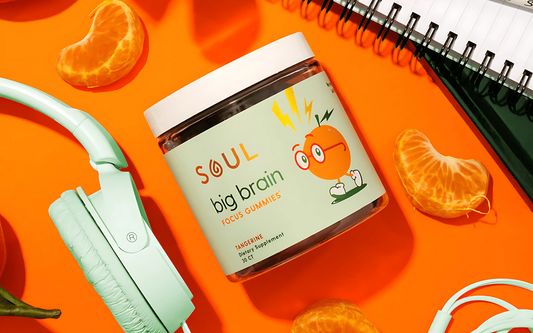 Angled view of Soul Big Brain Focus Gummies jar showing tangerine label and mascot on bright orange background with mint green headphones