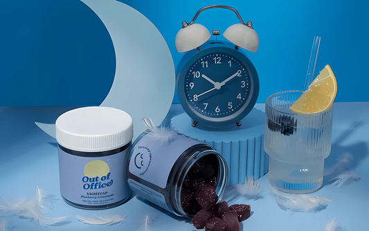 Tipped jar of CBD gummies spilling on a blue surface beside an alarm clock, paper crescent, feathers, and a lemon glass