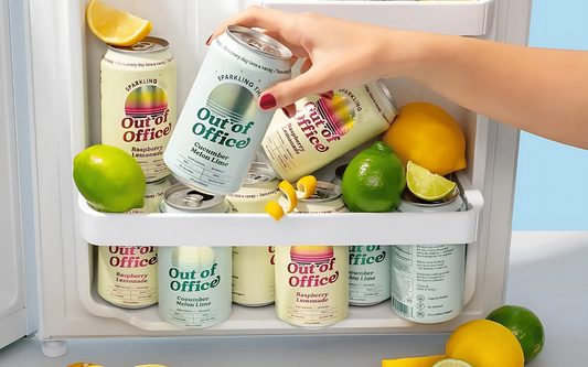 Close-up of Out of Office THC cans showing Cucumber Melon Lime and Raspberry Lemonade in a fridge with limes and lemons