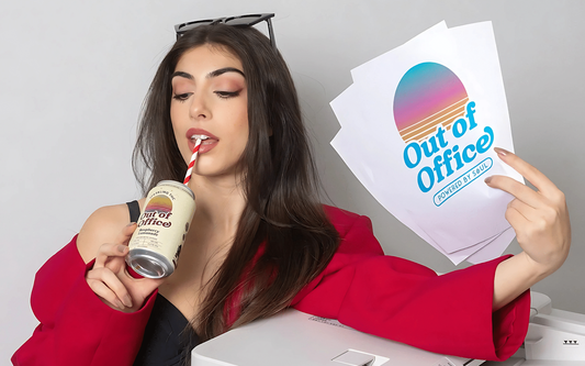 Woman in red blazer sipping a canned THC drink through a striped straw while holding papers that read ‘Out of Office’