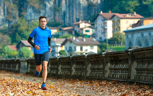 Man jogging on a leaf‑covered path beside a stone balustrade with village houses and cliffs in the background
