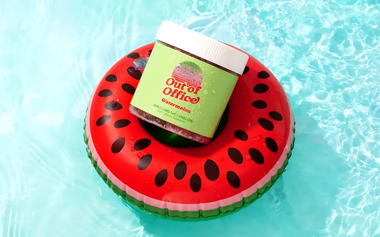 Angled overhead view of jar labeled ‘Out of Office Watermelon’ with water droplets, on a red watermelon float in a blue pool