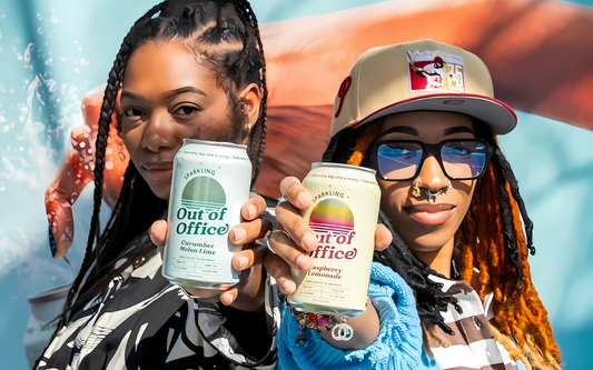 Two friends holding Out of Office sparkling cans, Cucumber Melon Lime and Raspberry Lemonade, outdoors