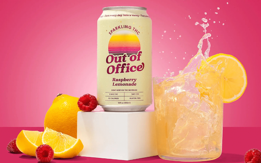 Front view of Out of Office Raspberry Lemonade THC can beside lemon, raspberries, and splashing glass on pink background
