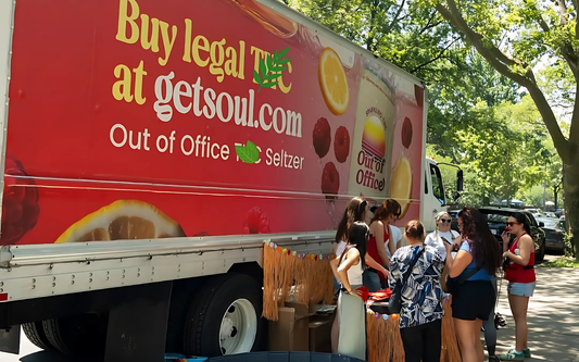 People gathered around a red promotional truck promoting getsoul.com Out of Office seltzer in a shaded park