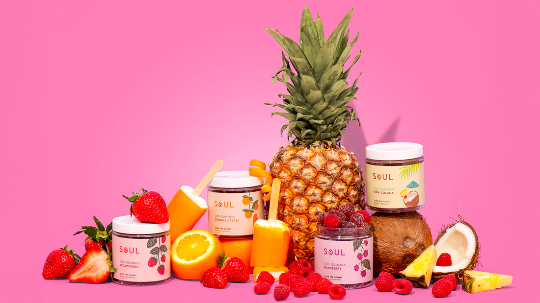 Front view of Soul CBD gummies jars showing flavor labels (strawberry, orange cream, raspberry, pina colada) with fruit on pink background