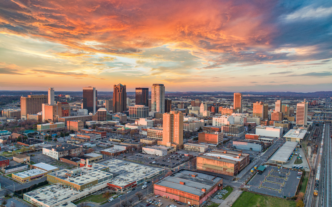 Aerial view of a city skyline at sunset with orange and pink clouds