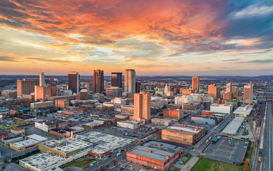 Aerial view of a city skyline at sunset with orange and pink clouds