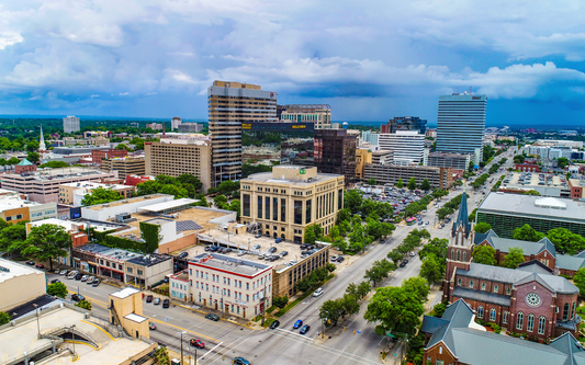 Aerial view of a downtown city center under a stormy sky, showing office towers, a church steeple, and tree-lined streets