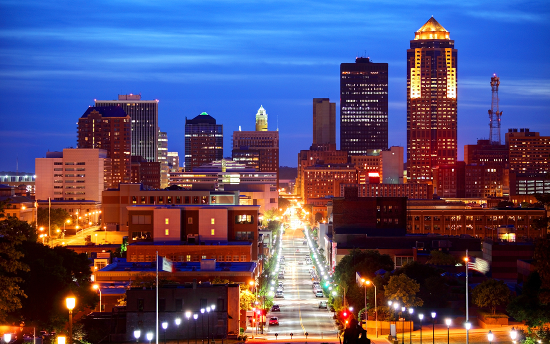 Iowa downtown skyline at dusk with illuminated high-rise buildings and a long, lamp-lined avenue leading into the city