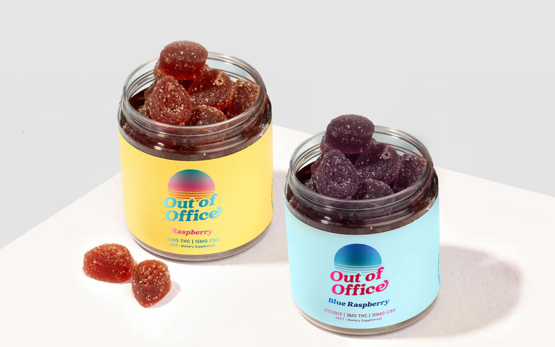 Angled view of two Out of Office gummy jars—raspberry (yellow label) and blue raspberry (light blue label)—open to show sugar-coated gummies on a white surface