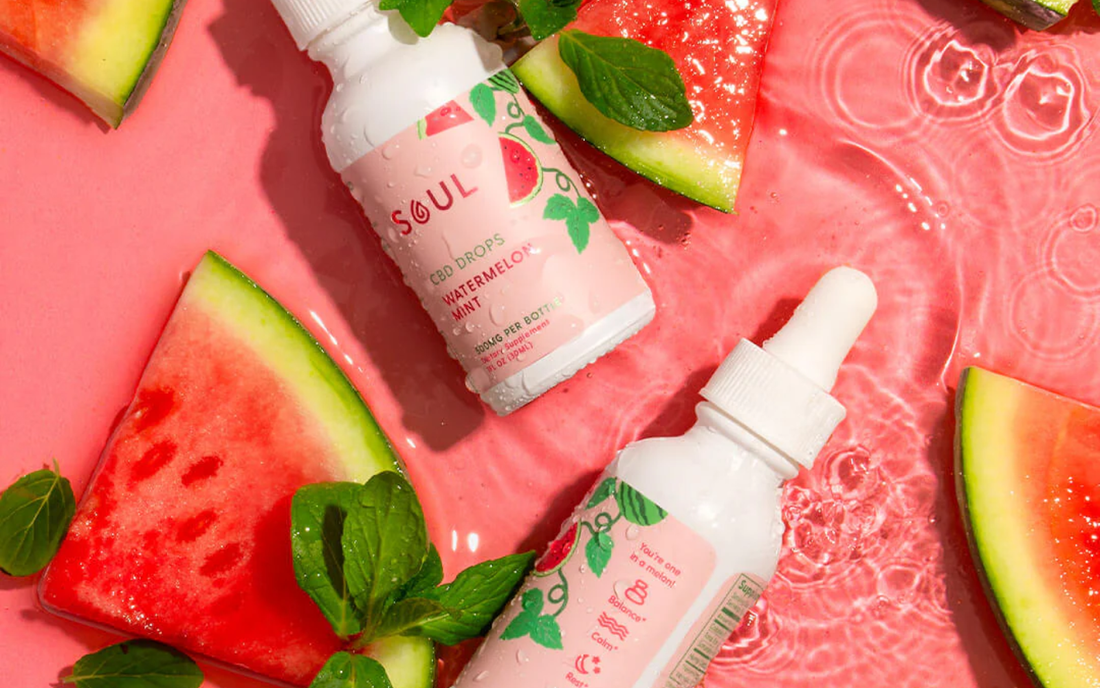 Angled view of Soul CBD Drops watermelon mint bottles showing dropper caps with watermelon and mint on pink background