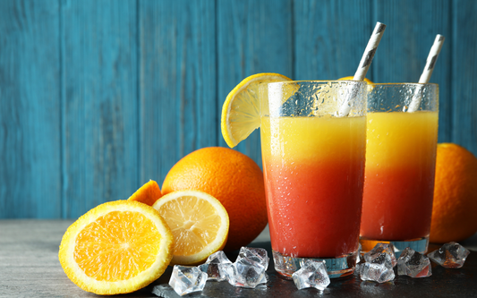 Two layered citrus mocktails with lemon wedges and striped paper straws on ice against a blue wooden background