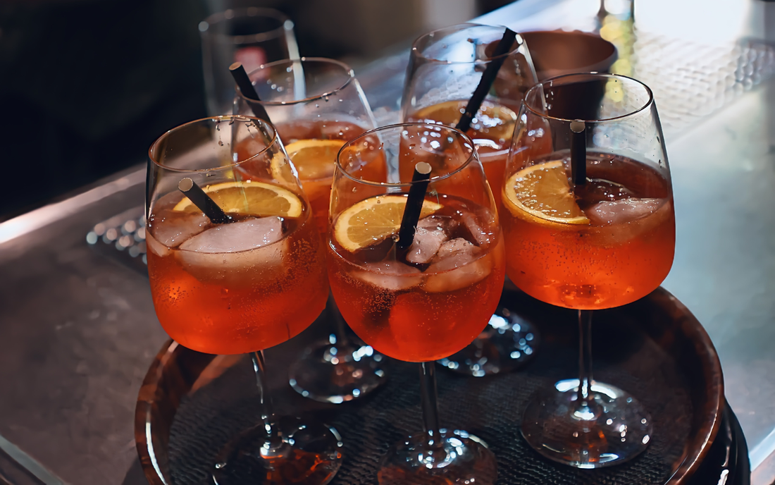 Group of orange cocktails in stemmed glasses with ice, lemon slices, and black straws on a bar tray