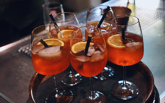 Group of orange cocktails in stemmed glasses with ice, lemon slices, and black straws on a bar tray