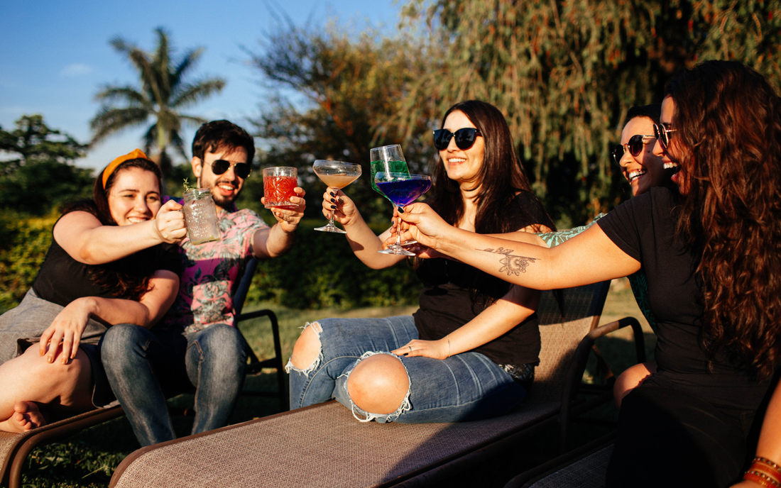 Five friends outdoors clinking colorful nonalcoholic drinks and laughing in a sunny backyard